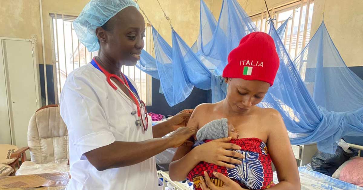A Sierra Leonean nurse pats the shoulder of a new mom who is holding her baby. 