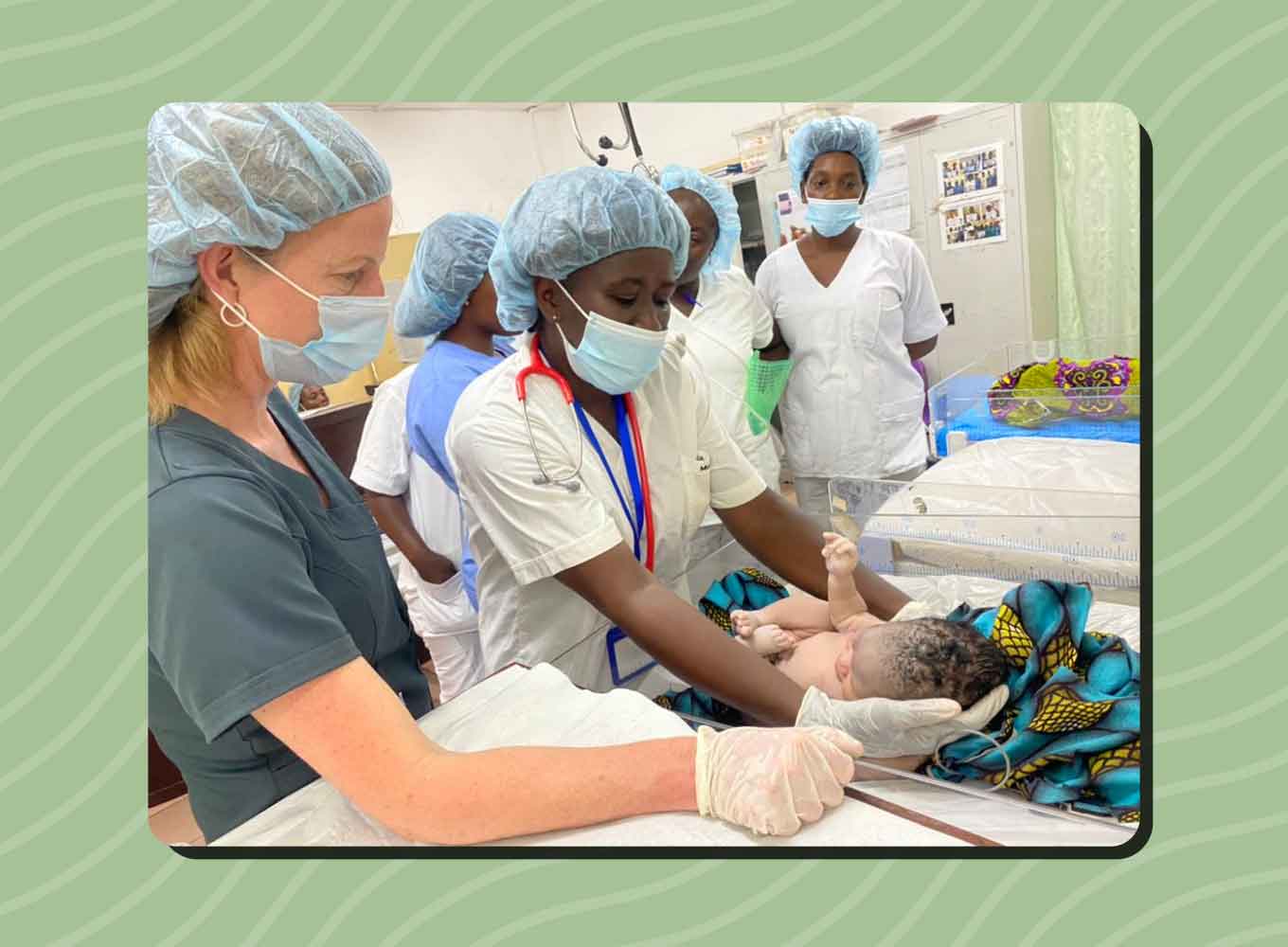 A white nurse stands beside a Sierra Leonean nursing student as she cares for a baby in a hospital.